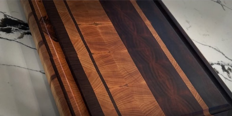 Striped end grain cutting board with a juice groove and integrated handle
